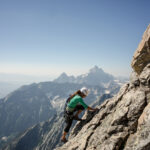 Climber scaling jagged mountain face with alpine view