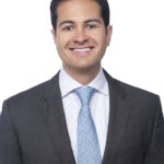 Smiling person in dark suit and blue tie